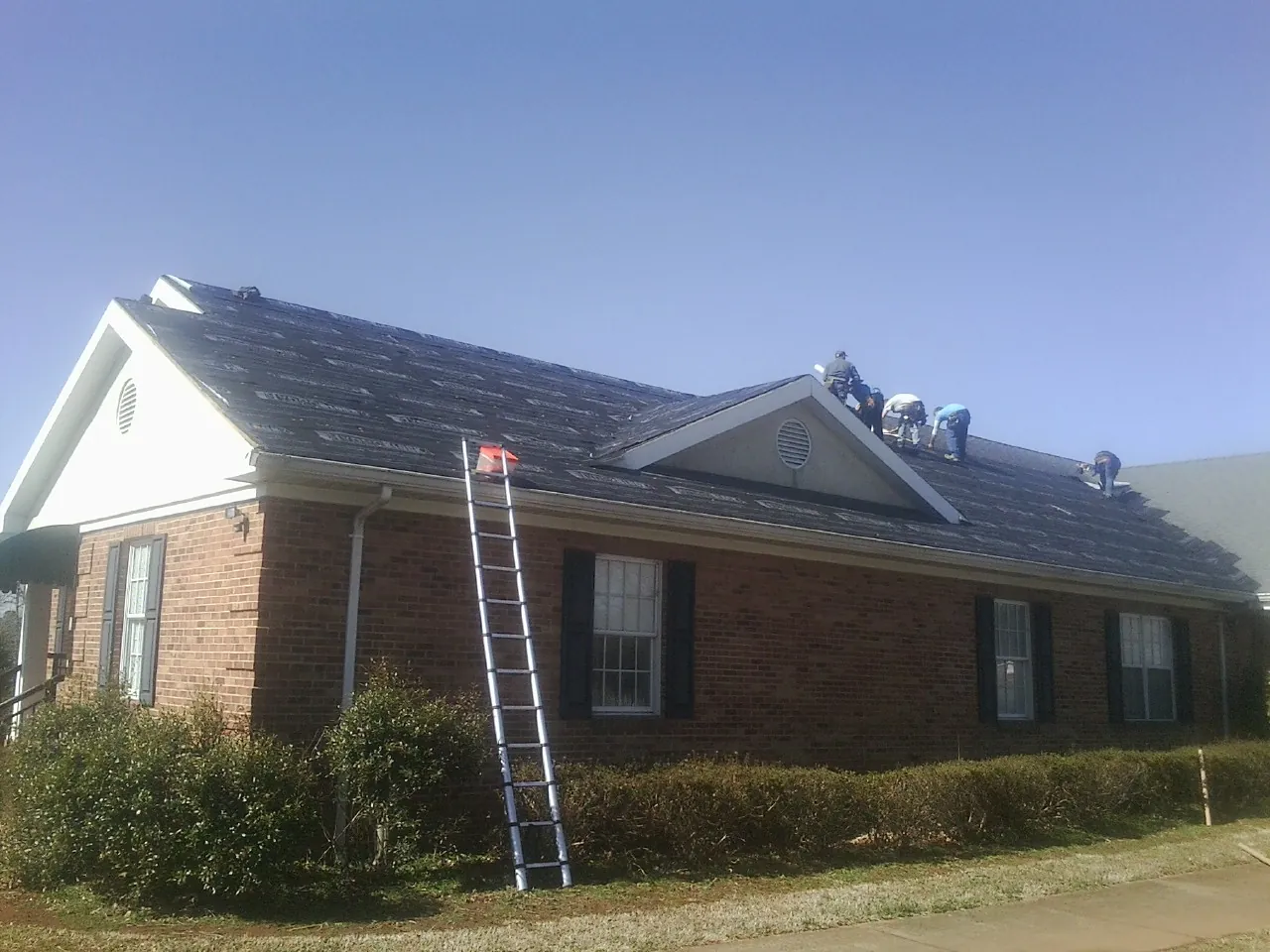 Crew tearing shingles off a brick ranch roof with a ladder set — Metal Roof Repair work by our crew in Lakeside Marblehead