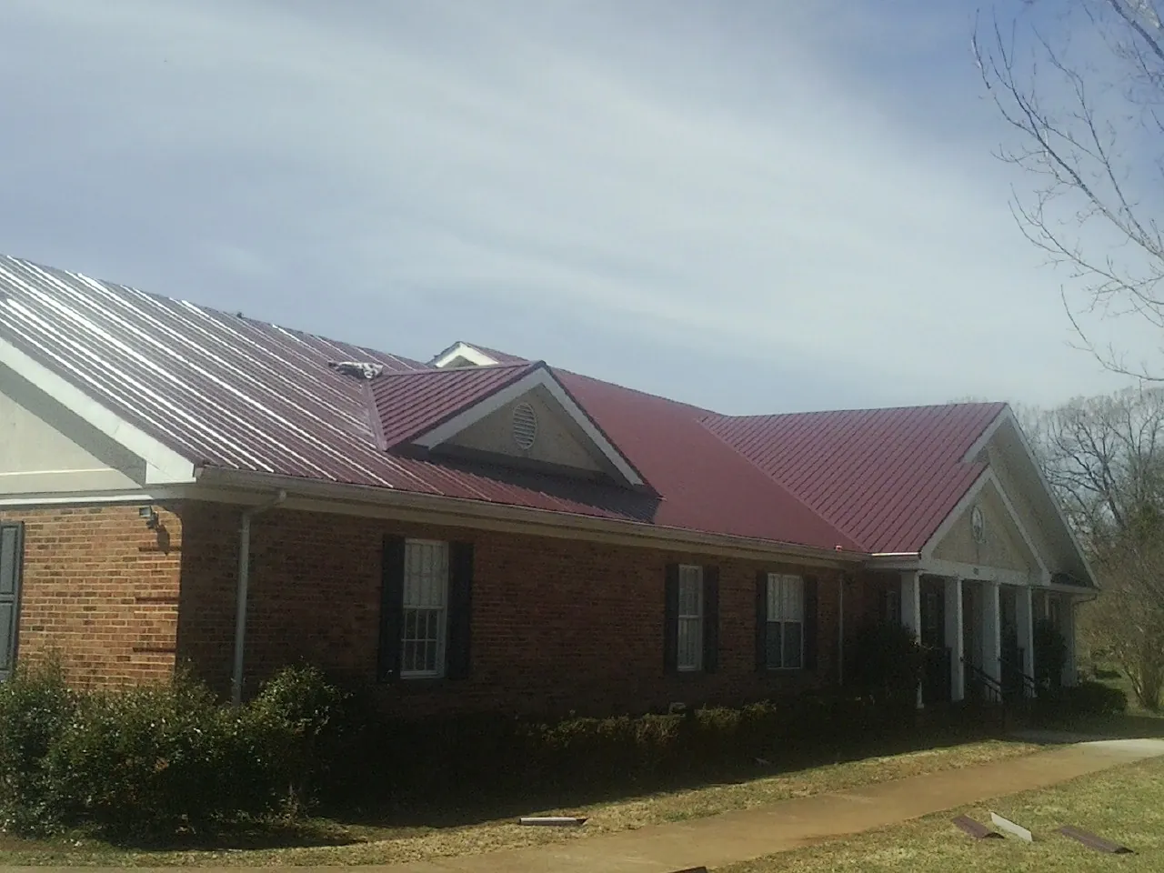 Red metal roof with gabled entries on a long brick building, from a Hail Damage Roof Repair job in Lakeside Marblehead