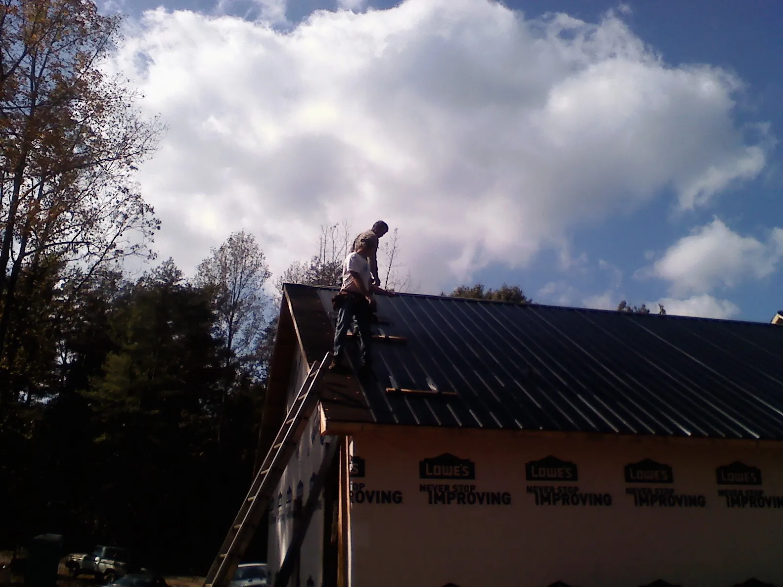 Roofer fastening dark metal panels high against a cloudy sky, from a Roof Inspection job in Lakeside Marblehead