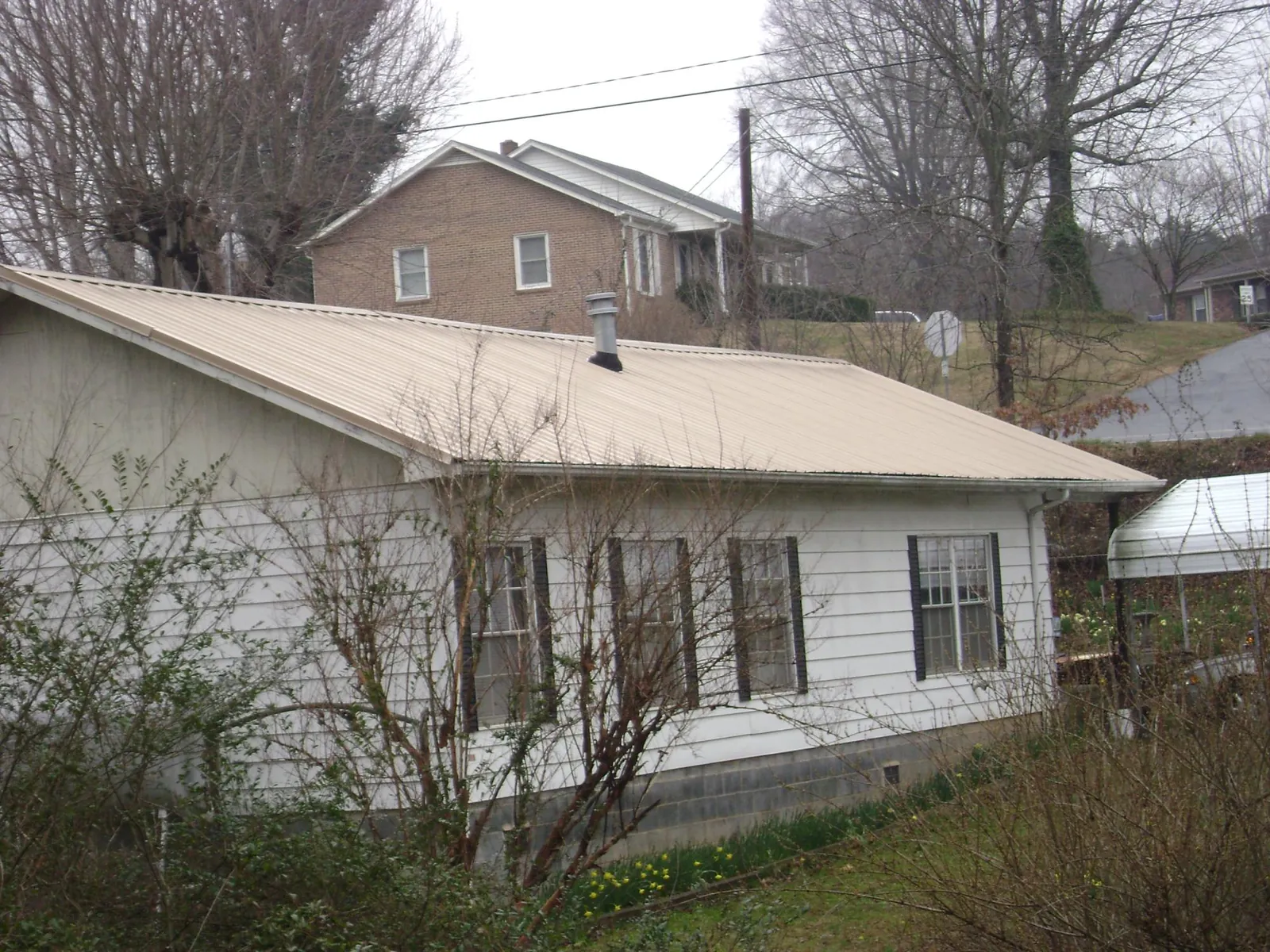 Tan metal roof on a white sided house set into a hillside — Commercial Roofing by Roofing Brothers in Lakeside Marblehead